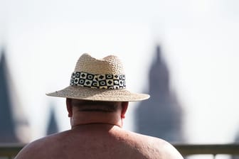 Ein Mann sitzt mit Hut am Rheinufer (Symbolbild): Empfindliche Menschen sollten keine anstrengenden Tätigkeiten verüben.