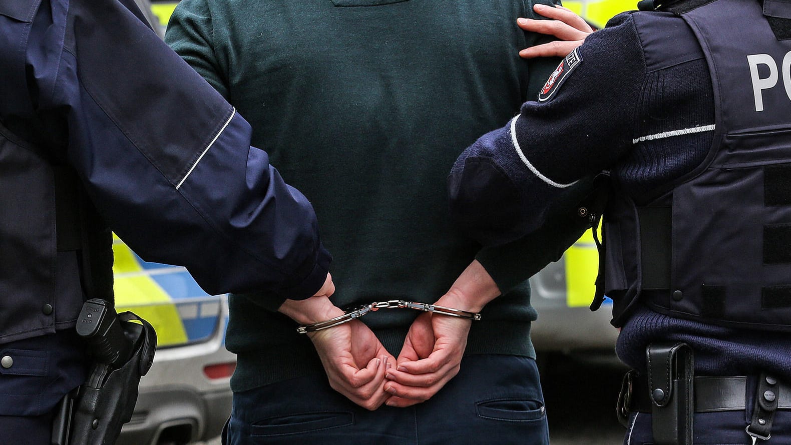 Zwei Polizisten mit einem Mann in Handschellen (Symbolbild): In Leverkusen hat die Polizei einen per Haftbefehl Gesuchten gestellt.