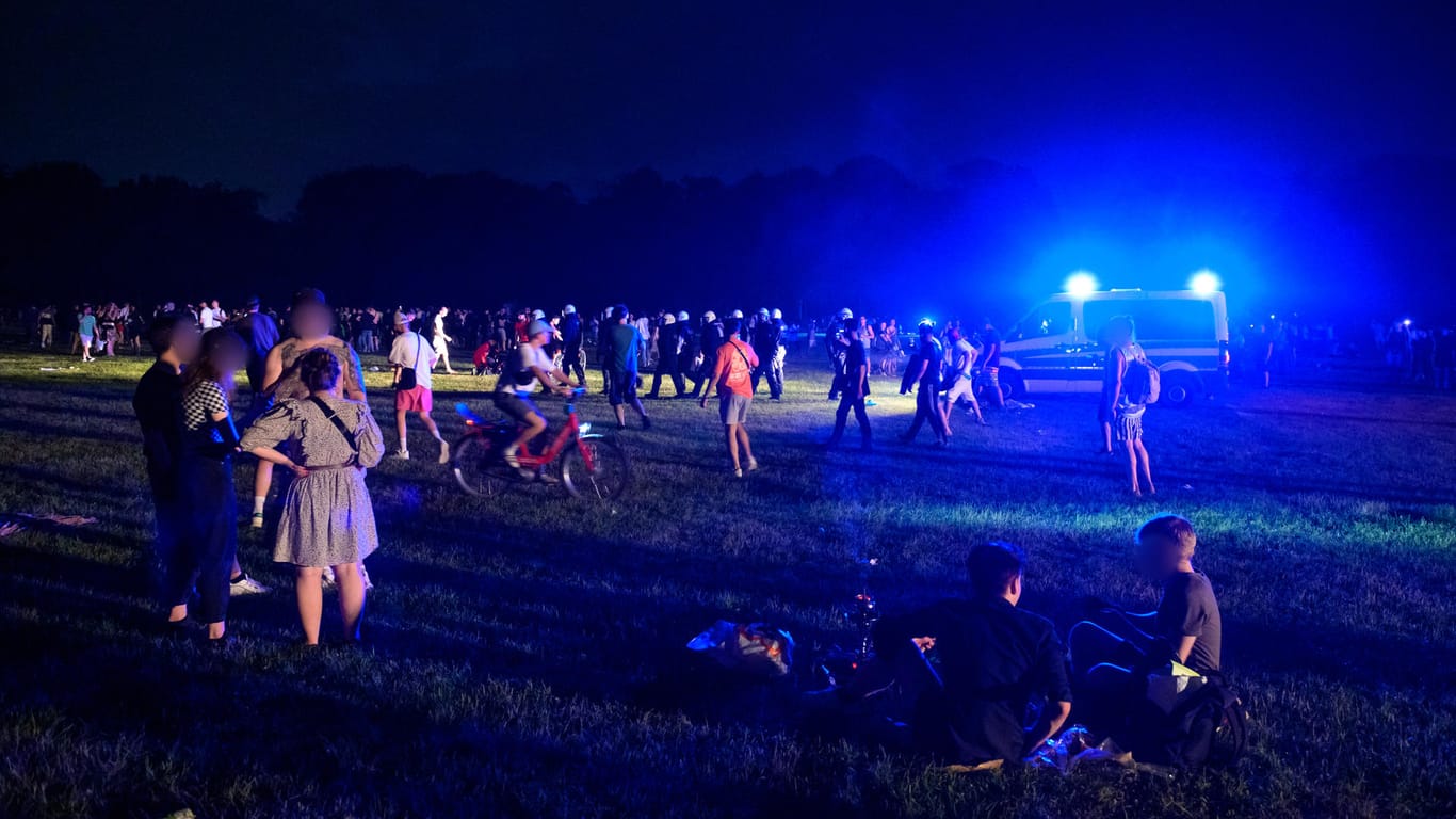 Menschengruppen auf der Stadtpark-Wiese – im Hintergrund behelmte Polizisten und ein Mannschaftswagen: Die Polizei hat eine Party auf der Grünfläche aufgelöst.