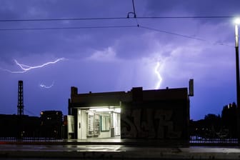 Unwetter in Teilen NRWs: Ein Blitz hellt zwischen einer Oberleitung einer Düsseldorfer Straßenbahn und einer Haltestelle auf.