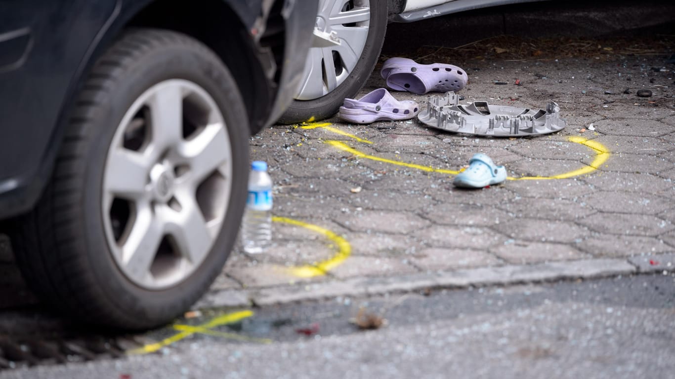 Schuhe, Fahrzeugteile und eine Trinkflasche stehen in Spurenmarkierungen zwischen den Unfallfahrzeugen.