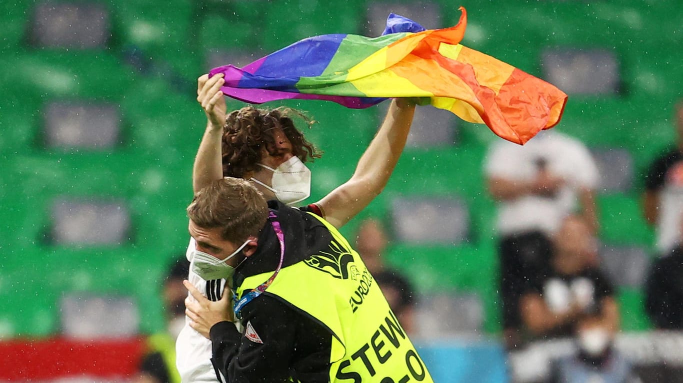 Ein Steward führt den Flitzer ab: Der junge Mann stellte sich mit der Regenbogen-Flagge vor die ungarische Mannschaft.