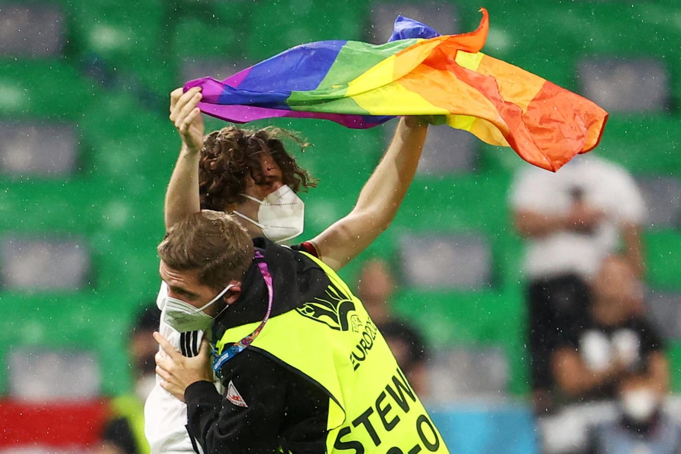 Ein Steward führt den Flitzer ab: Der junge Mann stellte sich mit der Regenbogen-Flagge vor die ungarische Mannschaft.