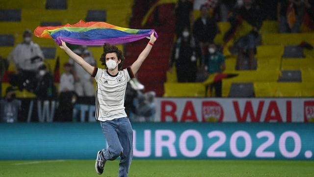 Ein junger Mann rennt mit einer Regenbogenfahne über das Spielfeld.