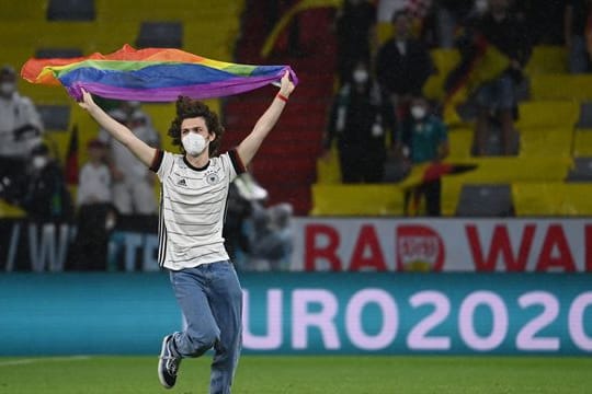 Ein junger Mann rennt mit einer Regenbogenfahne über das Spielfeld.