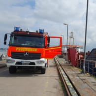 Ein Einsatzfahrzeug der Feuerwehr steht im Hafen neben dem Schüttgutfrachter. Für die Löscharbeiten musste das Schiff zunächst in einen anderen Hafen verlegt werden.