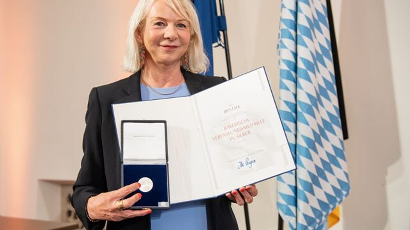 Rita Falk, Autorin, hält bei der Verleihung der Bayerischen Verfassungsmedaille im Landtag ihre Urkunde und Medaille in den Händen.