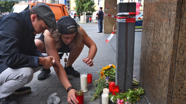 Messerattacke in Würzburger Innenstadt: Zwei junge Männer entzünden vor einem geschlossenen und abgesperrten Geschäft in der Innenstadt eine Kerze.