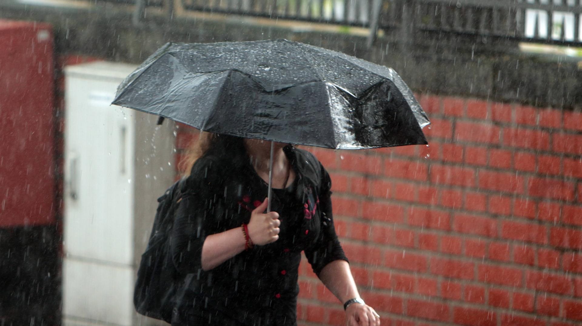 Eine Frau ist mit Regenschirm unterwegs am Rheinauhafen in Köln während eines Wolkenbruchs (Archivbild): Für NRW und Köln werden Unwetter erwartet.