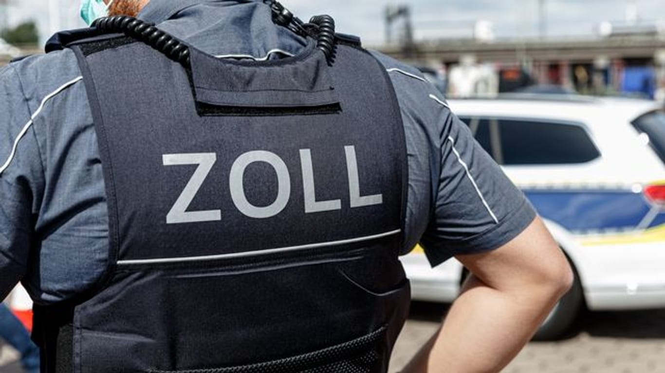 Ein Beamter trägt eine Schutzweste mit der Rückenaufschrift "Zoll" (Symbolbild): Der Zoll hat mehrere Gebäude durchsucht.