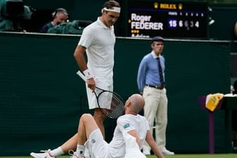 Roger Federer spricht mit Adrian Mannarino, der verletzt am Boden liegt.