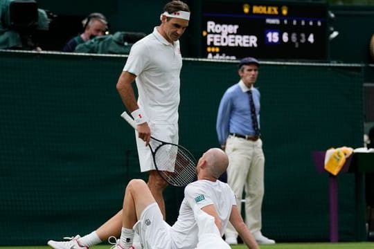 Roger Federer spricht mit Adrian Mannarino, der verletzt am Boden liegt.