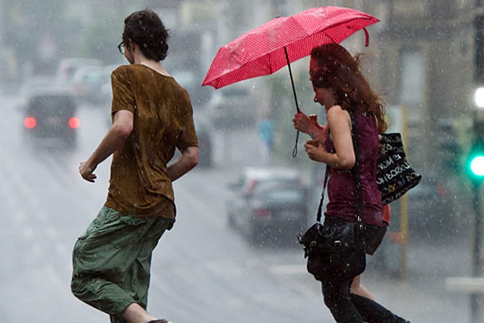 Junge Leute bringen sich in Stuttgart vor einem Platzregen in Sicherheit. Am Mittwoch regnet es langanhaltend.