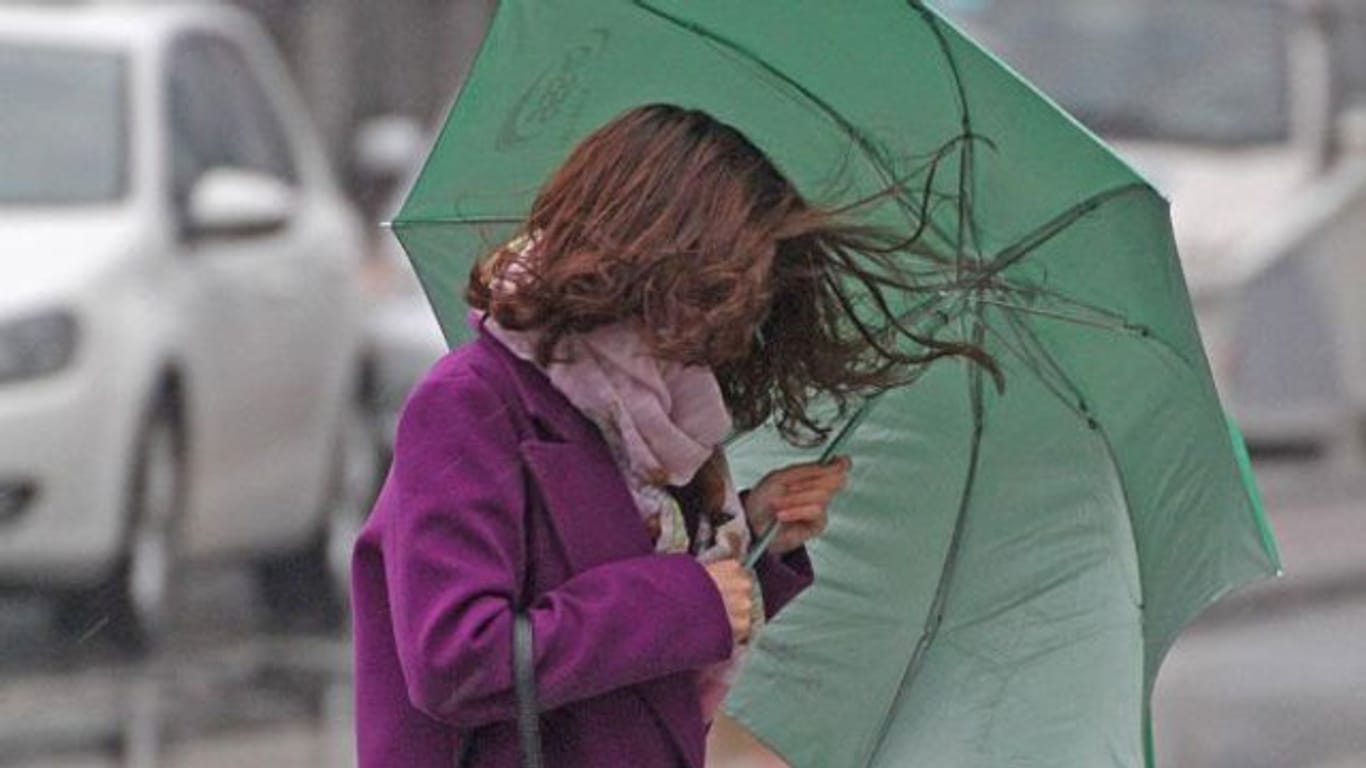 Mieses Wetter im Anmarsch: Eine Frau schützt sich vor Wind und Regen mit einem Schirm.