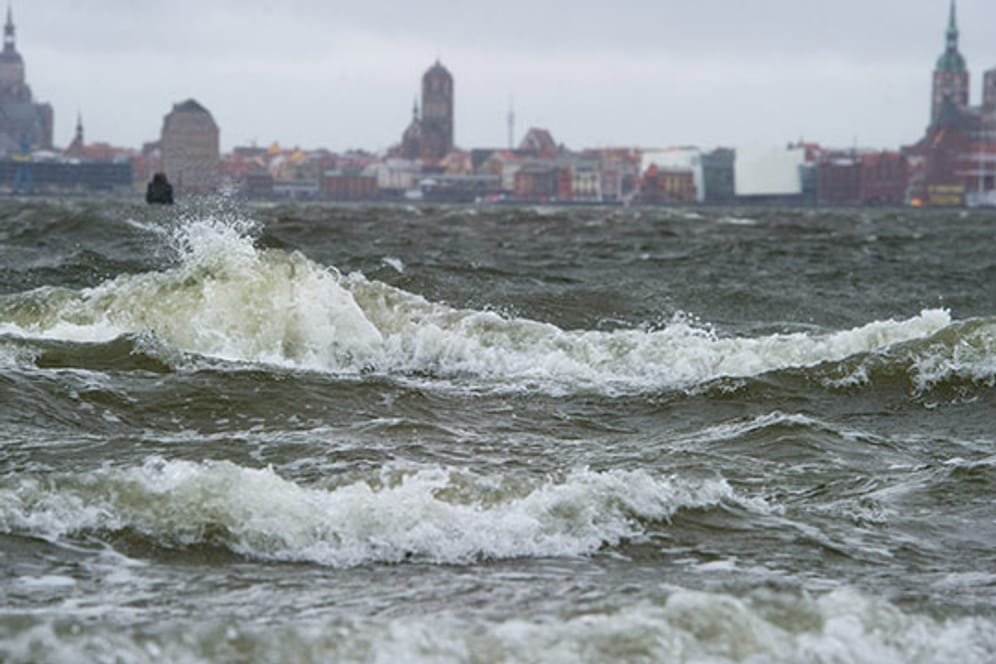 Wellen brechen sich am Strand von Altefähr auf der Insel Rügen. Im Hintergrund ist Stralsund zu sehen.