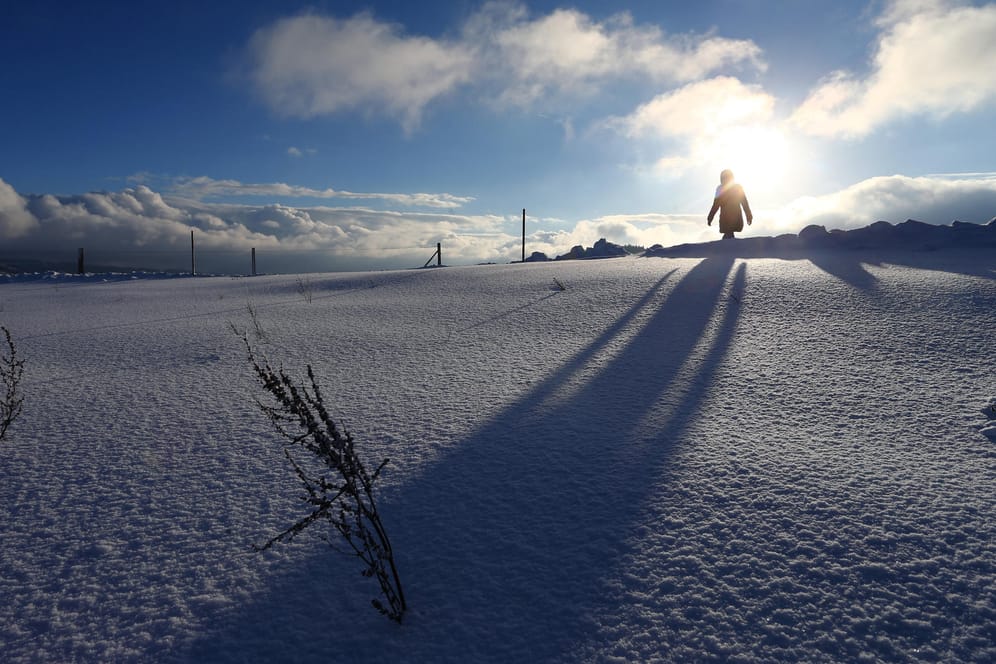 Schee: Eine Spaziergängerin läuft im Sonnenschein durch die tief verschneite Landschaft bei Scheidegg im bayerischen Allgäu.