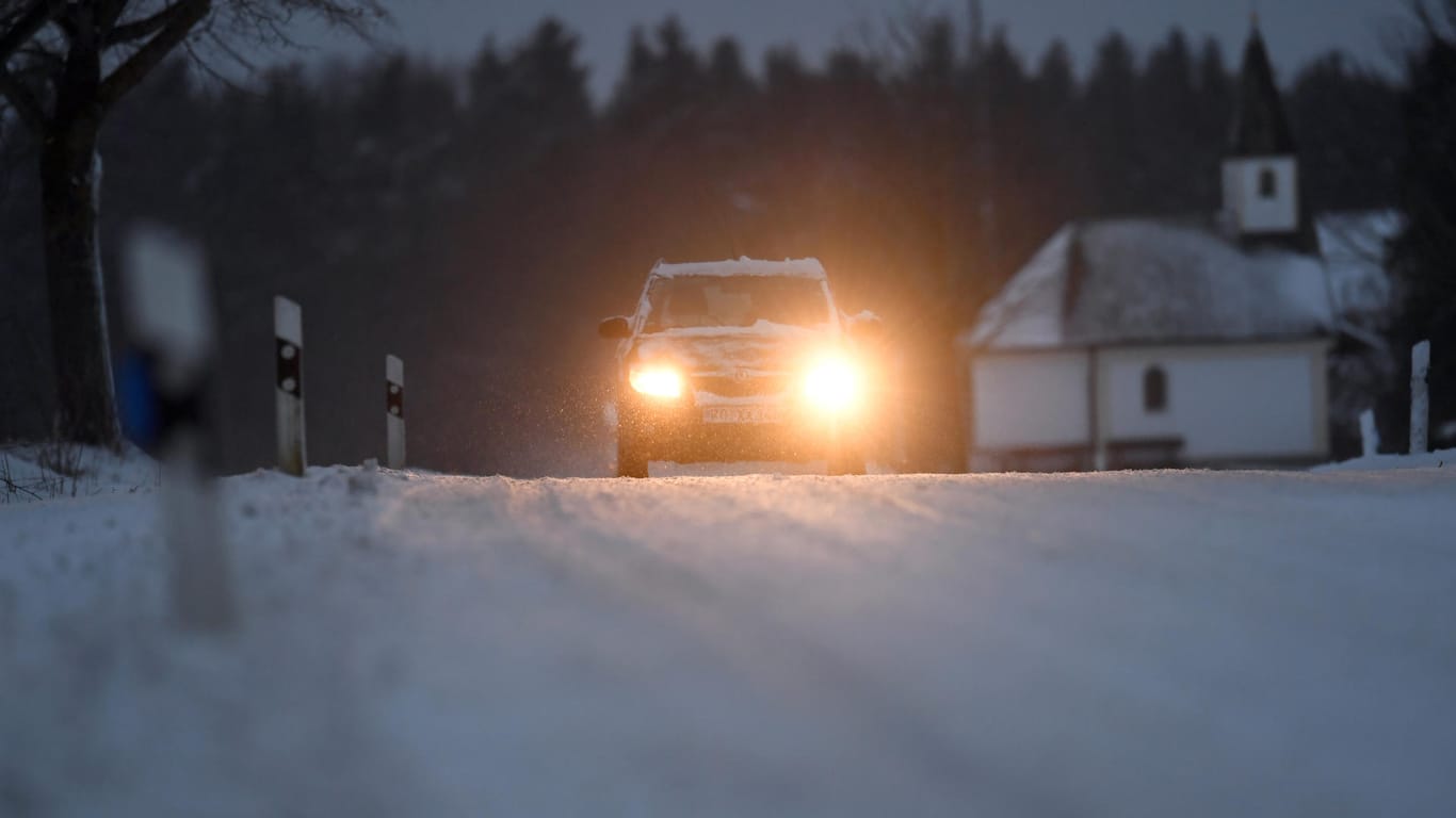 Ein Pkw fährt in der Nähe von Gollenshausen in Bayern über eine verschneite Straße.