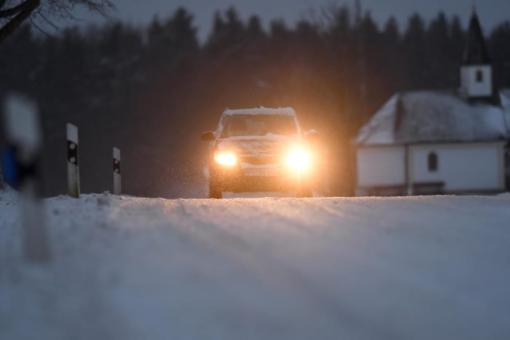 Ein Pkw fährt in der Nähe von Gollenshausen in Bayern über eine verschneite Straße.