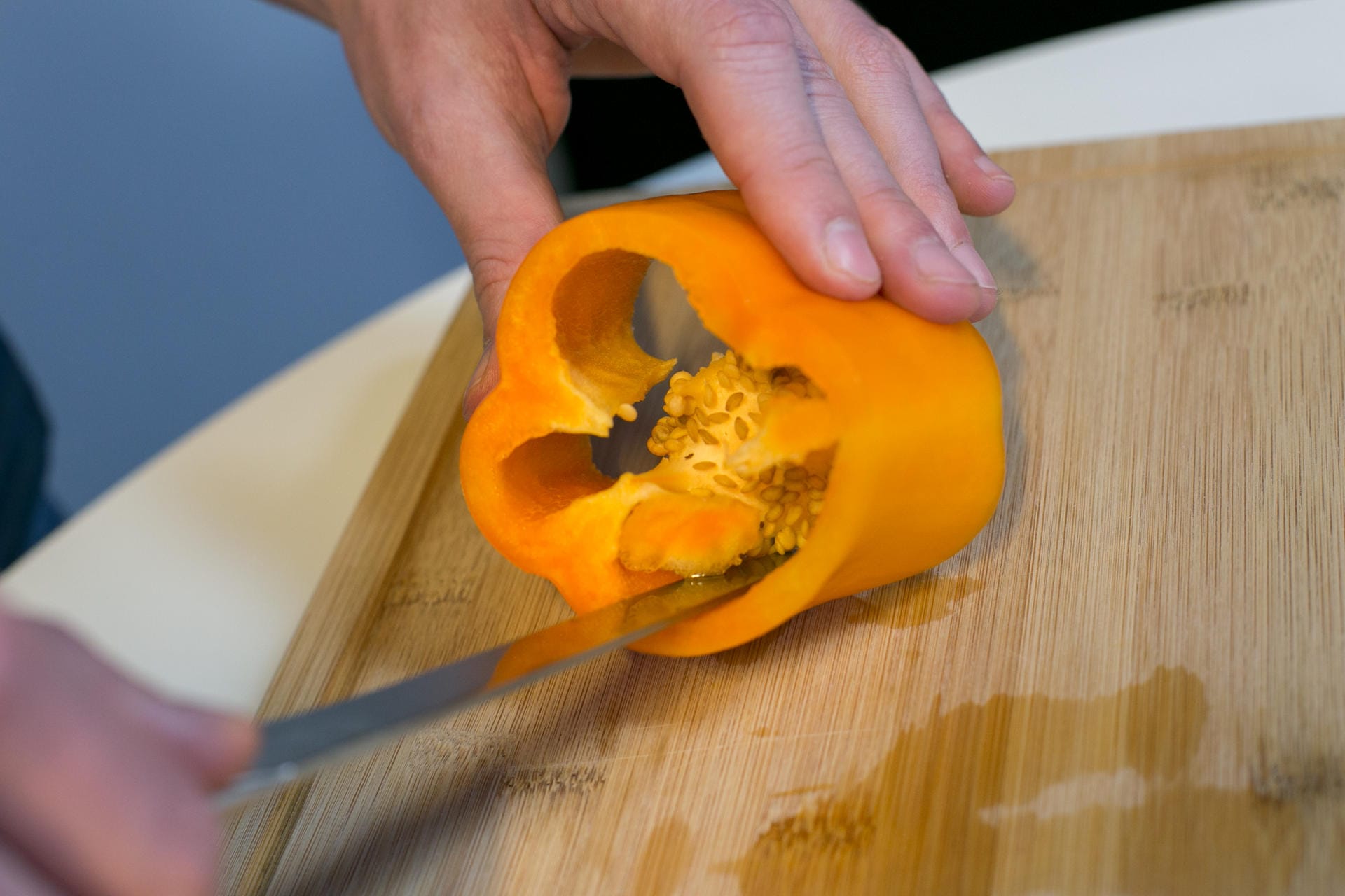 Schritt 3: Die Paprika mit einer Hand leicht schräg halten. Mit dem Messer in der anderen Hand das Kerngehäuse rundherum herausschneiden.