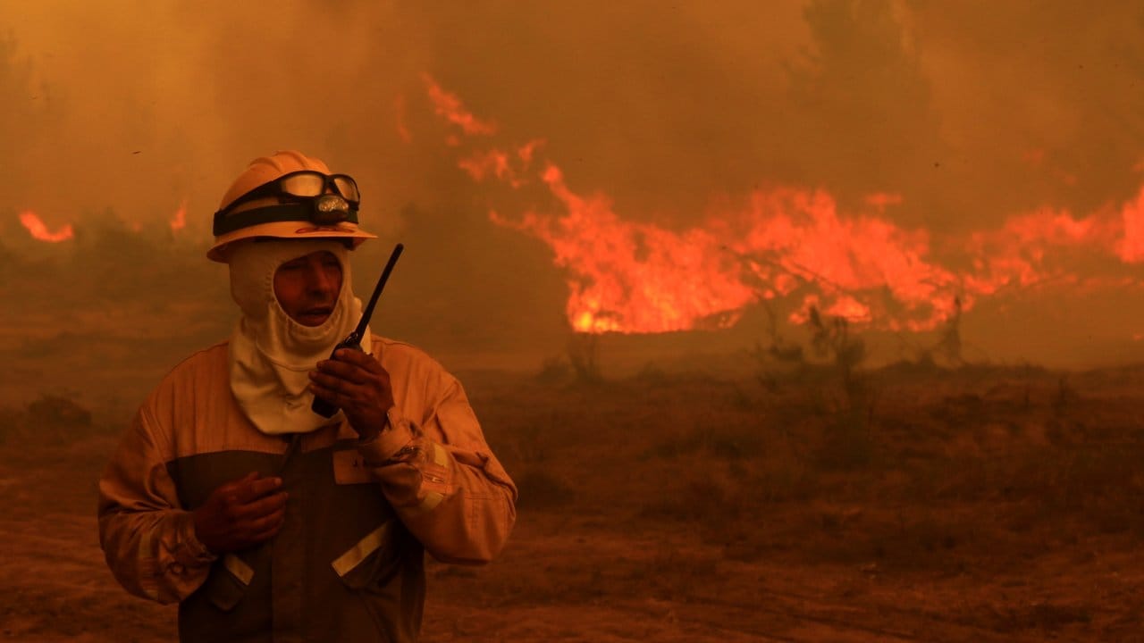 Ein Feuerwehrmann steht vor den lodernden Flammen des brennenden Waldes in Empedrado. Ein Feuerwehrmann steht vor den lodernden Flammen des brennenden Waldes in Empedrado.