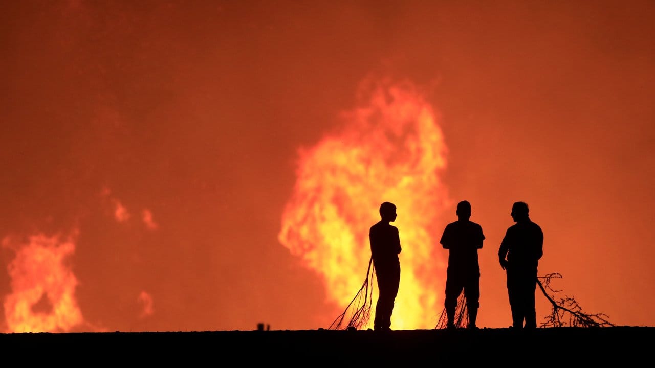 Bedrohliche Kulisse: Einsatzkräfte der Feuerwehr und Bewohner beobachten die Flammen. Bedrohliche Kulisse: Einsatzkräfte der Feuerwehr und Bewohner beobachten die Flammen.