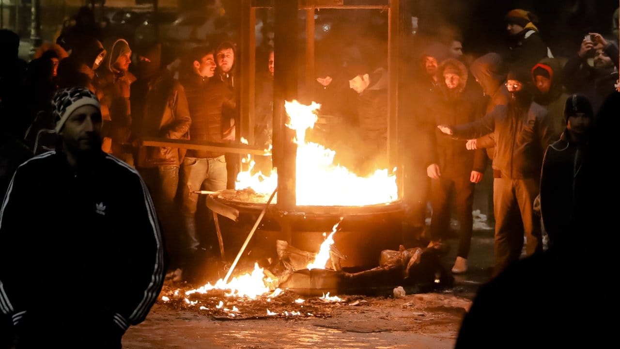 Demonstranten wärmen sich in Bukarest an einem brennenden Kiosk.