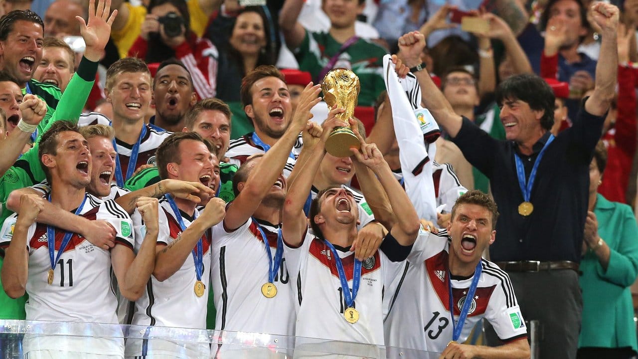Nach dem WM-Sieg hält Philipp Lahm (M) den Pokal über sich und teilt später dem Bundestrainer seinen Rücktritt aus der Nationalmannschft mit.