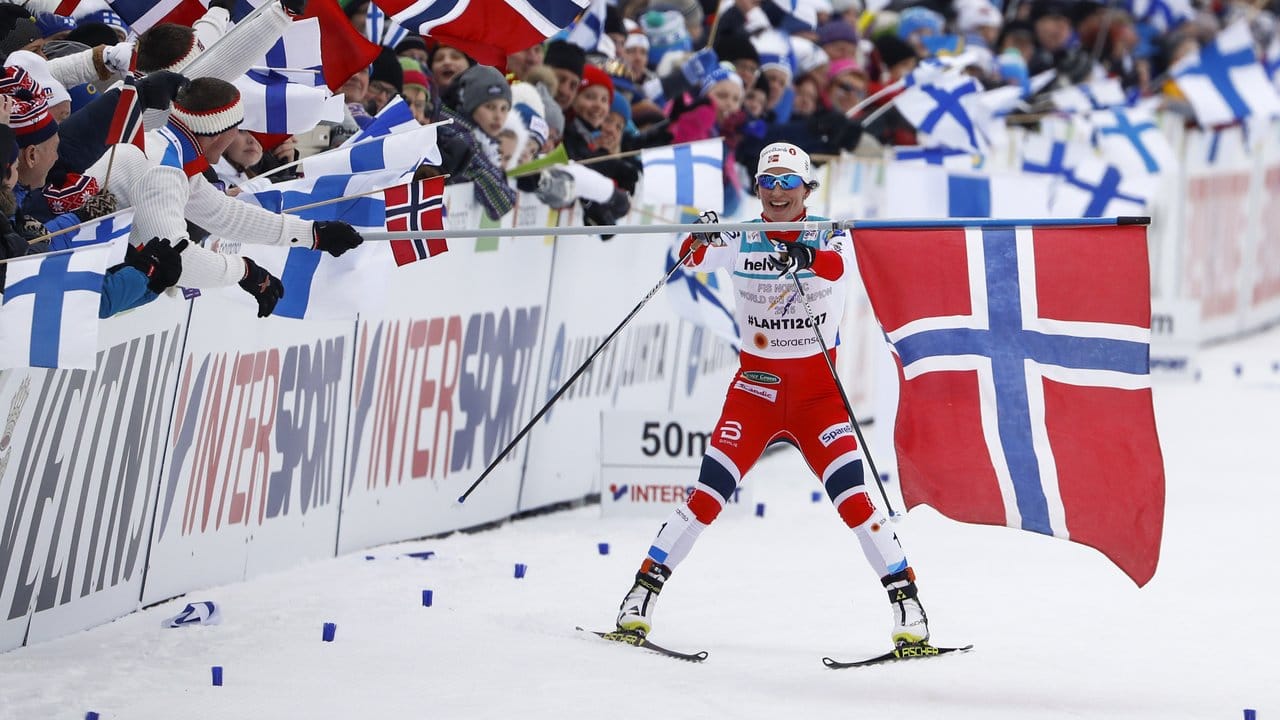 Die Norwegerin Marit Björgen nimmt sich als Schlussläuferin der Staffel auf den letztem Metern vor dem Ziel eine Fahne.