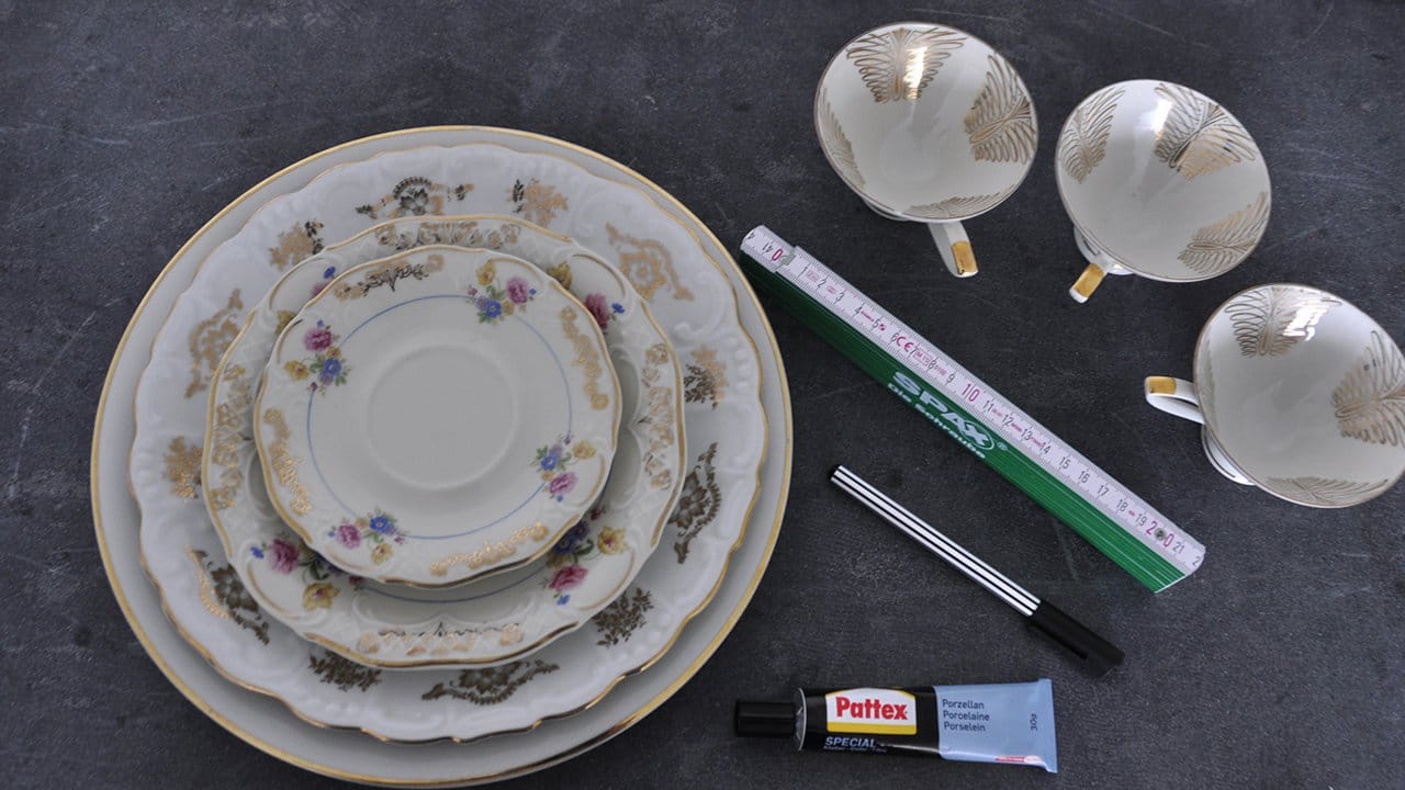 Das Material: Vier verschieden große Teller, drei Tassen, ein Zollstock, ein Filzstift und Porzellankleber. Das Material: Vier verschieden große Teller, drei Tassen, ein Zollstock, ein Filzstift und Porzellankleber.