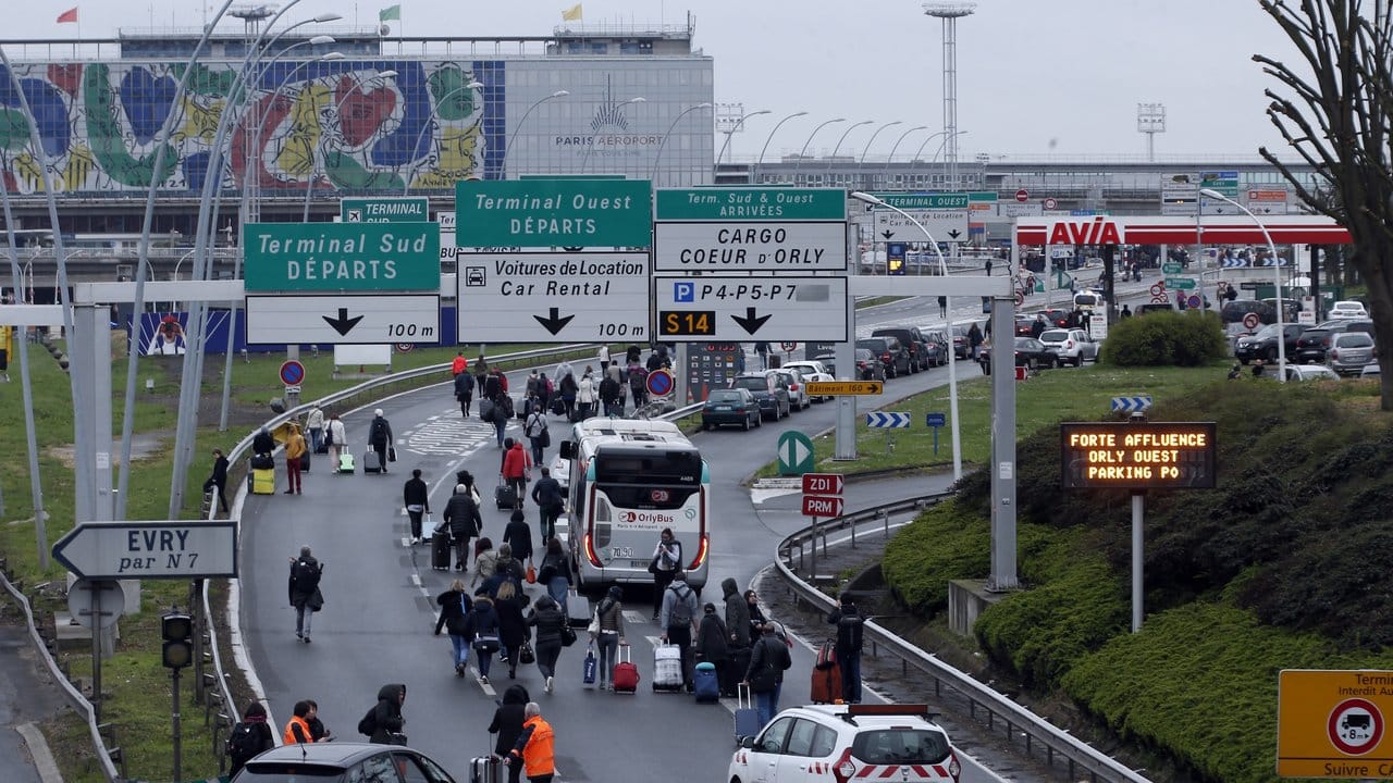 Reisende laufen mit Gepäck über die Autobahn zum Pariser Flughafen Orly.