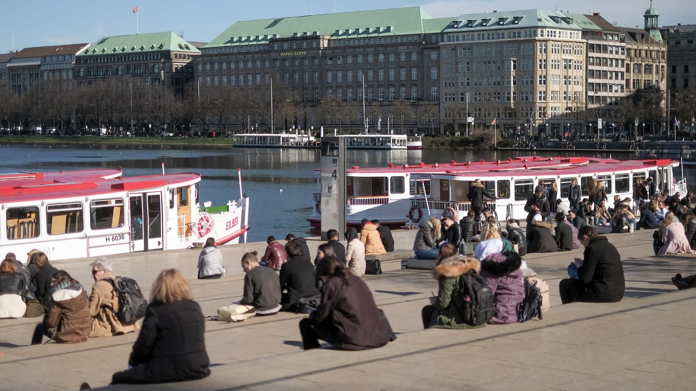 Frühlingswetter in Hamburg: Passanten sitzen am Ufer der Binnenalster in der Sonne.