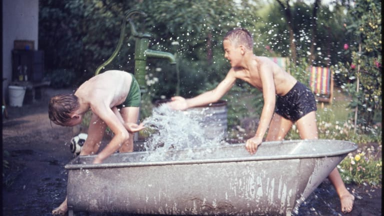 Zwei Jungs bespritzen sich im Garten mit dem Wasser aus einer Badewanne