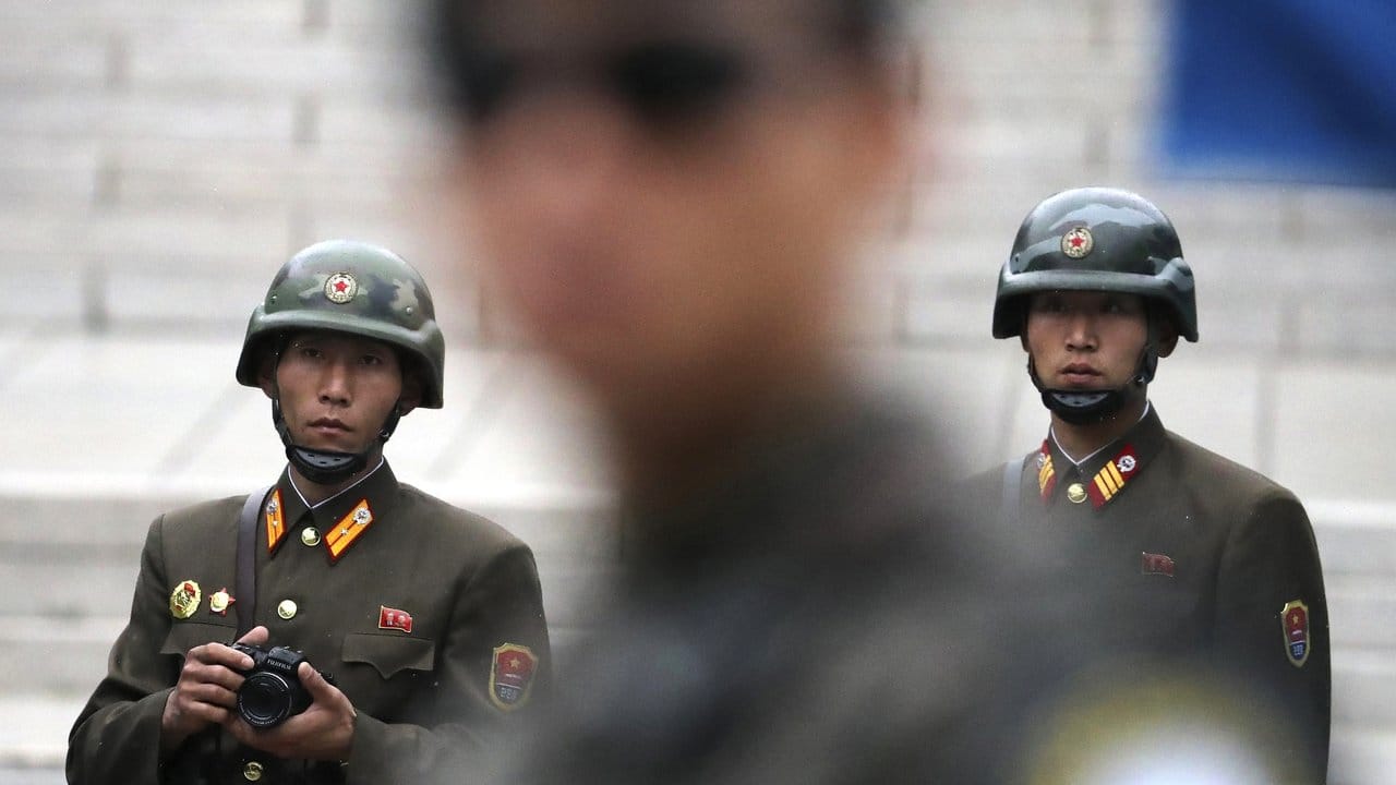 Zwei nordkoreanische Soldaten (hinten) blicken auf die Südseite wo ein südkoreanischer Soldat (M) Wache steht. Zwei nordkoreanische Soldaten (hinten) blicken auf die Südseite wo ein südkoreanischer Soldat (M) Wache steht.