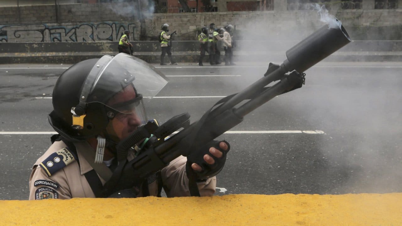 Ein Polizist feuert Tränengas in Richtung protestierender Demonstranten.