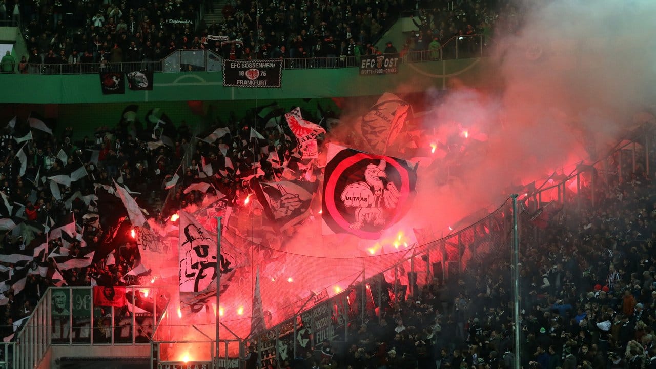 Ultras von Eintracht Frankfurt brennen zum Spielbeginn Pyrotechnik ab und schwenken Fahnen.
