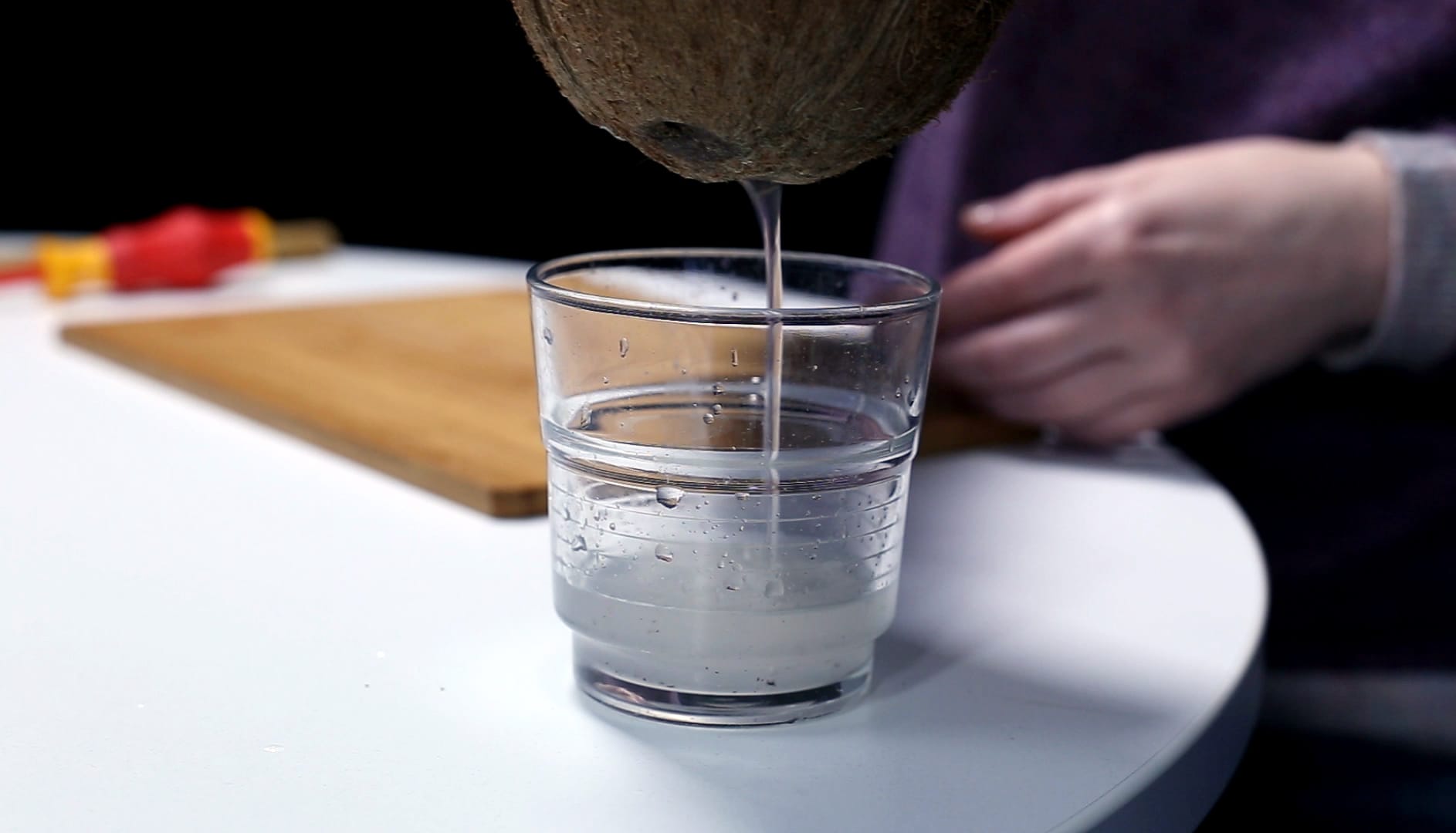 Kokosnuss: Schritt 2 – Aus den gebohrten Löchern das Kokoswasser in einem Glas auffangen.