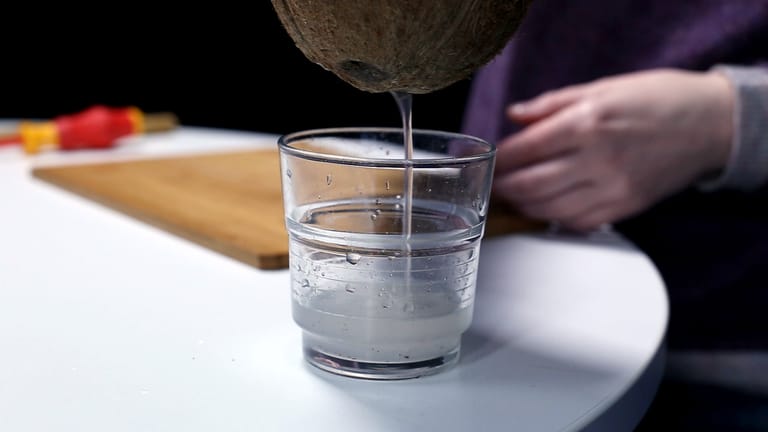 Kokosnuss: Schritt 2 – Aus den gebohrten Löchern das Kokoswasser in einem Glas auffangen.