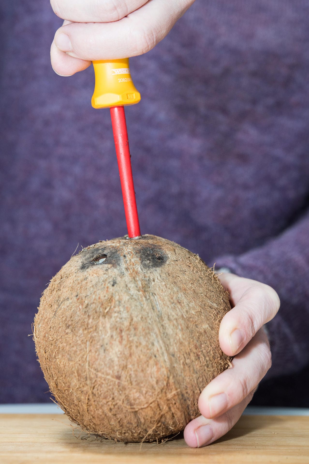 Kokosnuss: Schritt 1 – Mit einem Schraubenzieher in zwei der schwarzen Stellen der Kokosnuss ein Loch bohren.