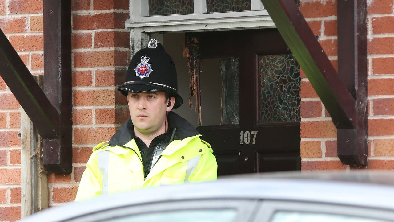 Ein Polizist steht vor einem Haus in Manchester, dessen Tür bei einer Durchsuchung beschädigt wurde. Ein Polizist steht vor einem Haus in Manchester, dessen Tür bei einer Durchsuchung beschädigt wurde.