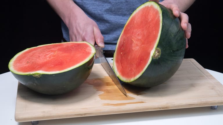 Die Messerklinge nach unten durchdrücken, sodass die Melone in zwei Hälften geteilt wird.
