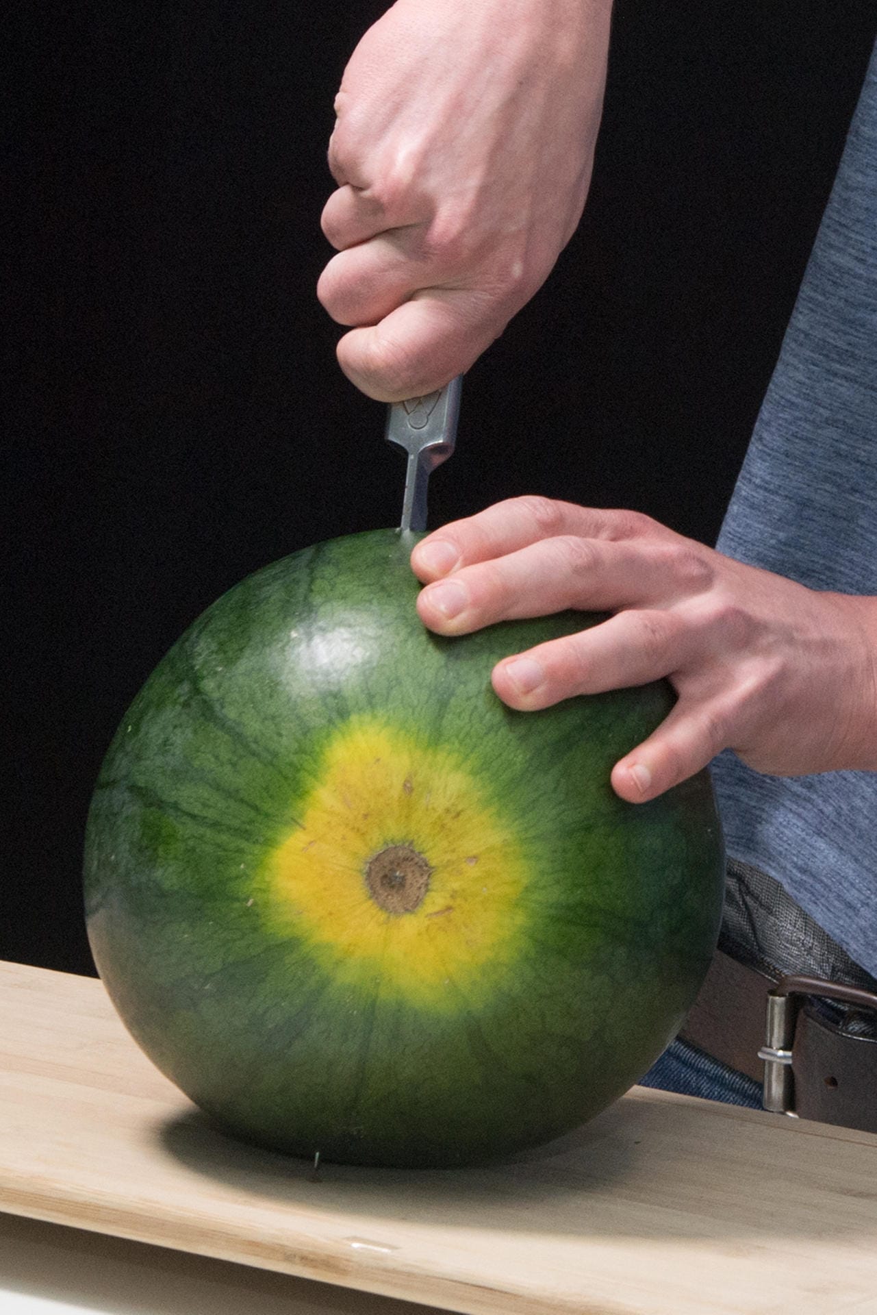 Wassermelone aufs Brett legen und mit einer Hand festhalten. Mit der anderen ein langes, spitzes Messer senkrecht in die Frucht stechen.