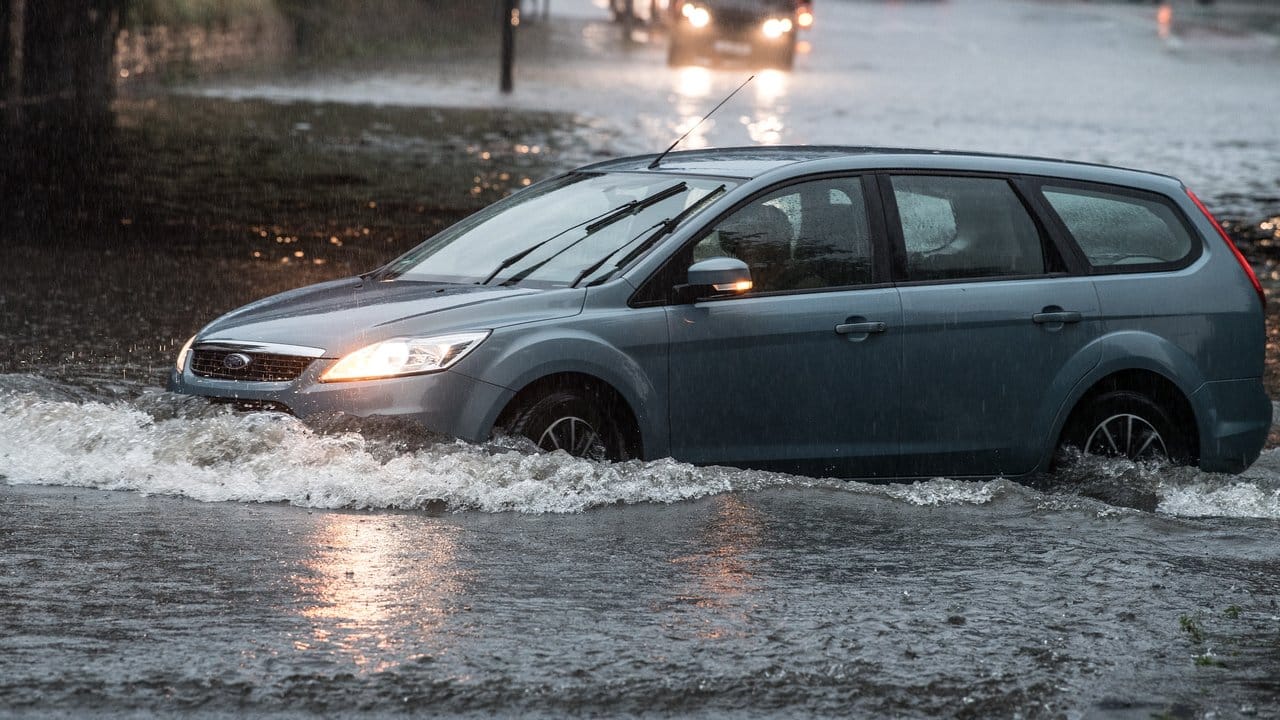 Ein Auto fährt auf einer überfluteten Straße in Köln.