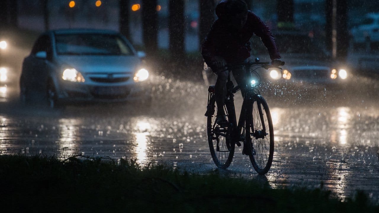 Ein Fahrradfahrer und Autos fahren bei einem Unwetter mit Starkregen auf einer Straße in Hannover.