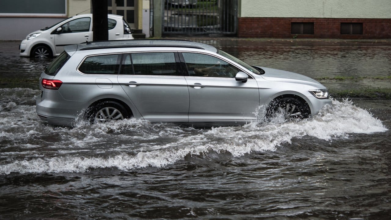 Ein Pkw fährt in Berlin nach einem Gewitter und starken Regenfällen durch Wassermassen.