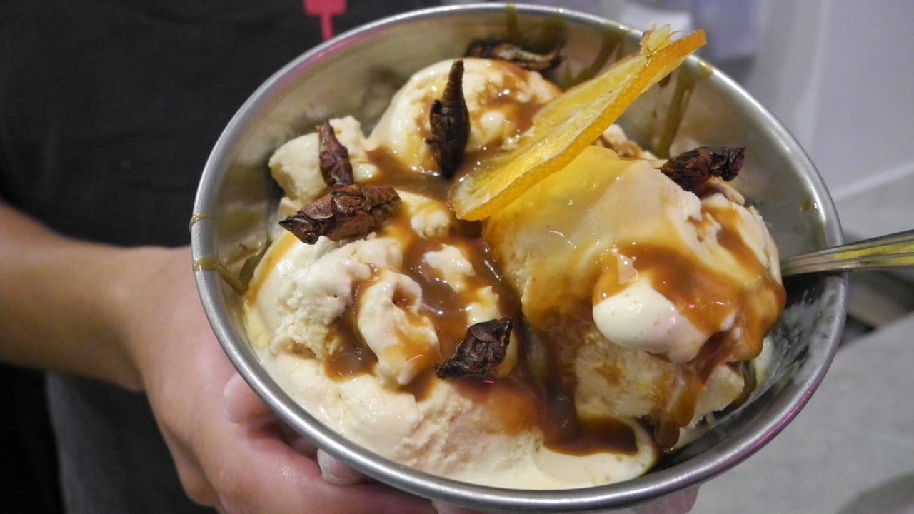 Der Eisbecher „Happy Hoppy“ besteht aus Vanilleeis, das mit Chipotle-Chili angereichert wurde, aus Mezcal-Caramel, einer kandierten Orangenscheibe und gerösteten Heuschrecken.