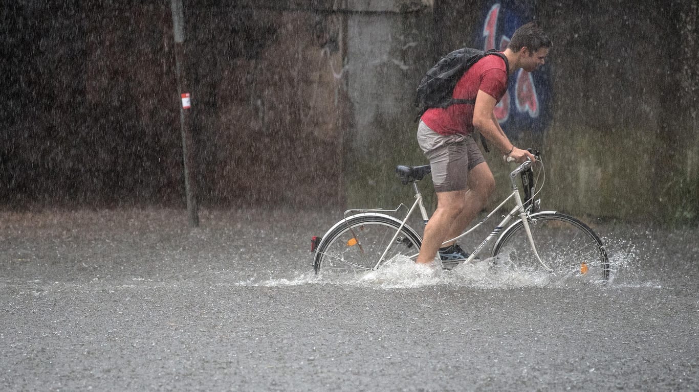 Ein Fahrradfahrer fährt auf einer überfluteten Straße in Köln während eines Gewitters.