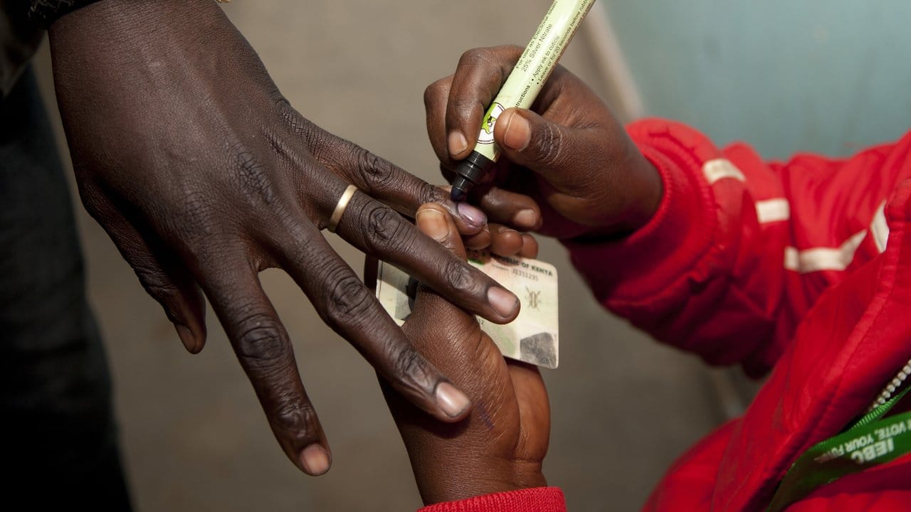 Eine Wahlhelferin markiert in einem Wahllokal den Finger eines Wählers, nachdem dieser seine Stimme abgegeben hat.