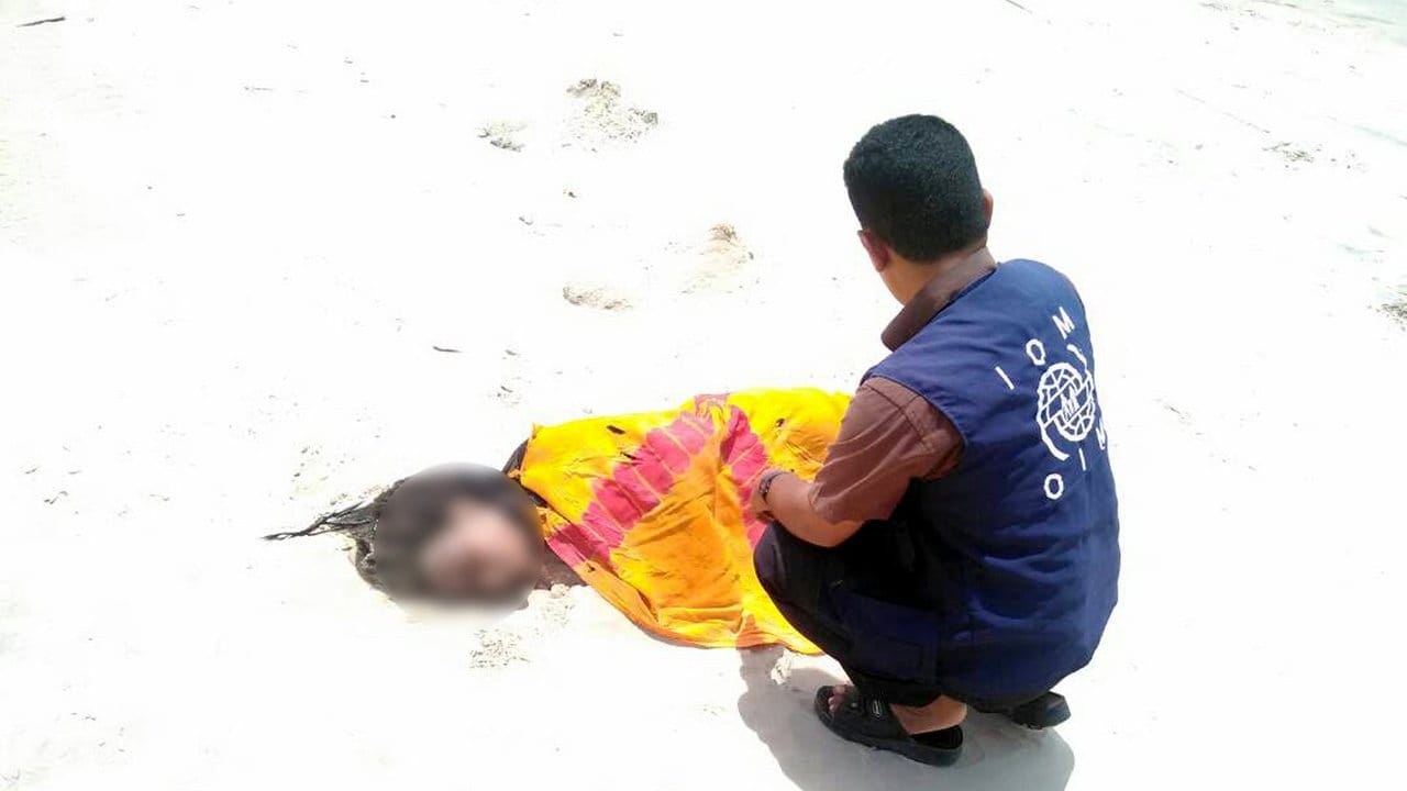 Ein Mitarbeiter der Internationalen Organisation für Migration (IOM) kniet an einem Strand im Jemen neben dem Leichnam eines ertrunkenen Flüchtlings.