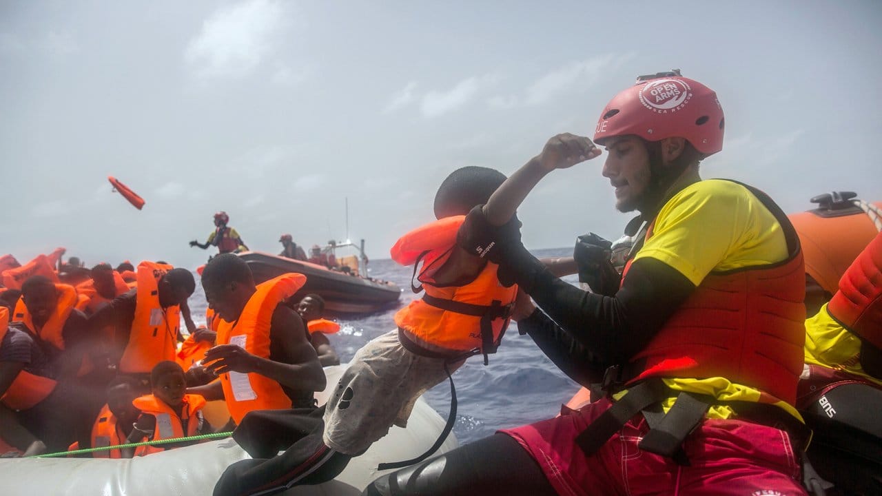 Ein Mitarbeiter der spanischen NGO "Proactiva Open Arms" hebt vor der libyschen Küste ein Kind aus einem überfüllten Flüchtlingsboot.