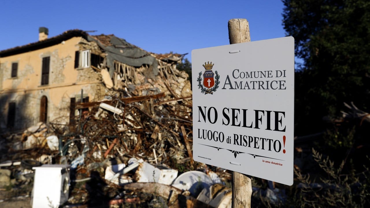 Ein Hinweisschild auf dem zu lesen ist, dass aus Respekt keine Selfies gemacht werden sollen, steht vor den Trümmern eines zerstörten Hauses in San Cipriano.